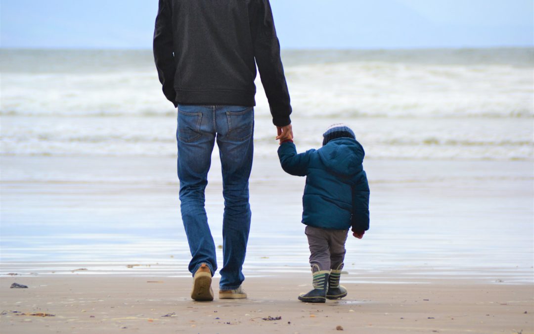 Dad holding sons hand on the beach. Picture gives the impression that the dad is telling his son something important. Fathers Day