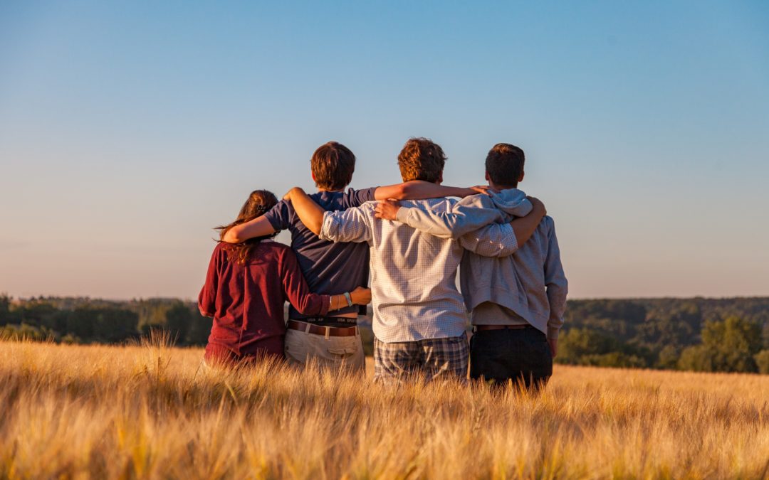 Group of four friends holding on to each other while looking out over a mountain landscape. The image communicates that each of them belong on this adventure.