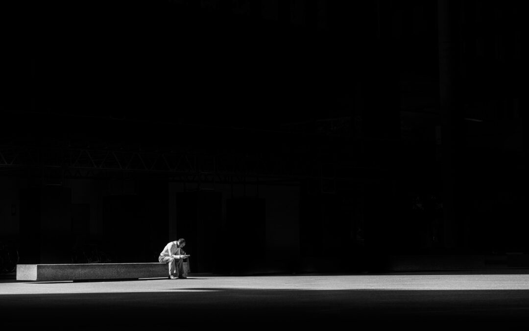 A man sitting alone in a dark room. One ray of light shines over him.